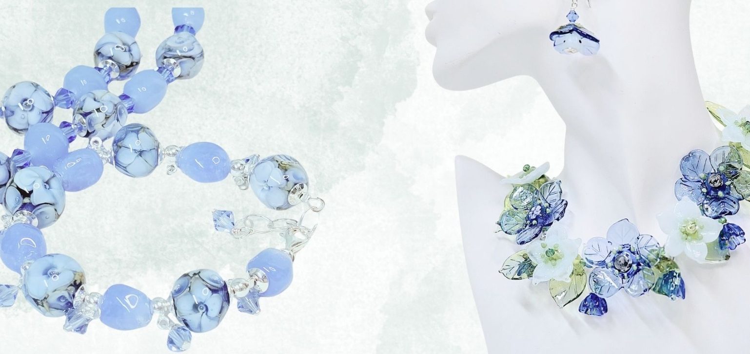 Blaue Schmuckstücke aus Glasperlen und floralen Elementen auf hellem Hintergrund.